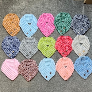 Könnte beinhalten: Eine Sammlung von 15 gehäkelten Halstüchern in verschiedenen Farben und Mustern, darunter Rosa, Blau, Grün, Braun und Weiß. Jedes Halstuch hat einen Knopfverschluss.