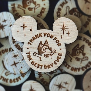 Könnte beinhalten: Holzausschnitte in Mickey-Mouse-Form mit eingraviertem Text und einem Cartoon-Hund. Der mittlere Ausschnitt lautet "THANK YOU FOR THE BEST DAY EVER". Weitere Ausschnitte zeigen denselben Text und Sternmuster.