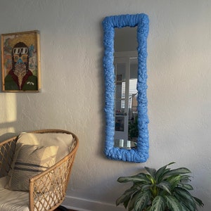 May include: A blue mirror with a unique, textured frame. The frame is made of a soft, pliable material that resembles foam. The mirror is rectangular and has a modern, abstract design.