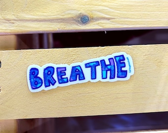 May include: A blue and white sticker with the word "BREATHE" in a decorative font. The sticker is on a wooden surface.