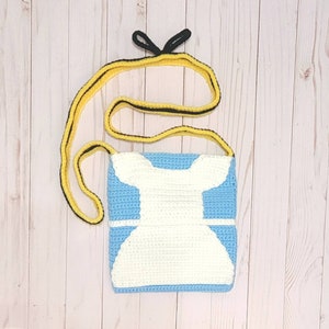 May include: A crocheted blue and white purse with a white dress design. The purse has a yellow and black strap.