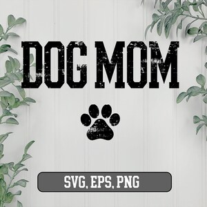 May include: Black and white graphic design with the text "DOG MOM" in a distressed font. A black paw print is below the text. The text "SVG, EPS, PNG" is at the bottom of the image.