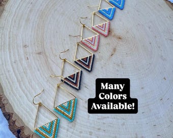May include: A collection of beaded earrings in various colors, including turquoise, pink, and brown, arranged on a wooden surface. Each earring features a geometric design within a gold-colored frame. The text "Many Colors Available!" is also visible.