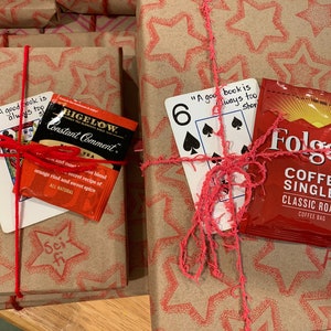 May include: Two wrapped gifts with red string and a star pattern. One gift has a tea bag and a card with the text "A good book is always too short". The other gift has a coffee bag and a card with the text "A good book is always too short" and the number 6.