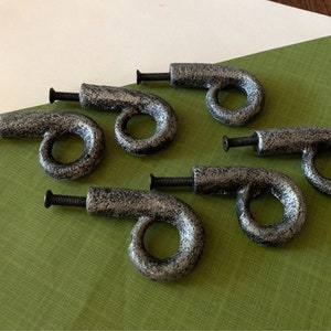 May include: Six silver-toned metal drawer pulls with a loop design. Each pull has a black screw.