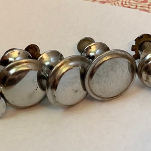May include: Five silver-toned cabinet knobs with a rounded, slightly domed shape. The knobs have a smooth, shiny finish and are attached to screws.