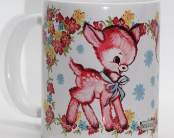 May include: White ceramic mug with a pink deer surrounded by colorful flowers. The deer has a blue bow and the mug has the word "MISERIA" printed on the bottom.