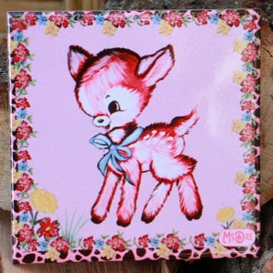Puede incluir: Un azulejo de cerámica rosa y blanco con un borde floral. El centro del azulejo presenta una ilustración de dibujos animados de un cervatillo rosa con un lazo azul. El azulejo está firmado "Ms. Rae".