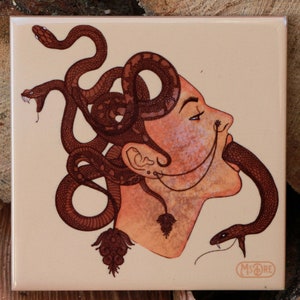 May include: A ceramic tile featuring a hand-drawn illustration of a person with snakes for hair. The person's face is turned to the side and they are biting a snake. The tile has a light brown background and the illustration is in shades of brown and orange.