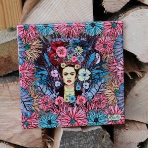 May include: A square tile featuring a colourful floral design with a woman wearing a flower crown. The woman has dark hair, dark eyes, and red lips. The tile is decorated in shades of blue, pink, and green.