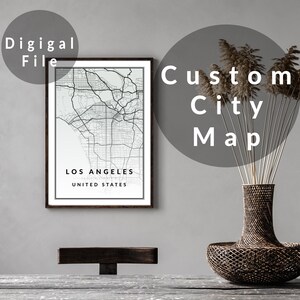 May include: A framed black and white map of Los Angeles, California, labeled "Digital File" and "Custom City Map." The map is displayed on a wall, with a decorative vase and dried plants in the foreground. The text "LOS ANGELES UNITED STATES" is visible.