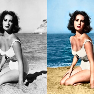 May include: A woman in a white swimsuit kneels on a sandy beach, with the ocean and a clear blue sky in the background. The image is a vintage photograph, with the woman's dark hair styled in a short bob. The swimsuit has a scoop neckline.