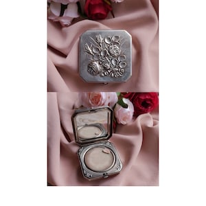 Peut inclure: Un poudrier argenté avec un motif floral sur le couvercle. Le poudrier est ouvert, révélant un miroir et une houppette à poudre blanche.