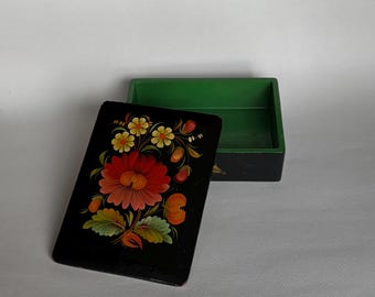 May include: A small, rectangular black box with a hinged lid, featuring a vibrant floral design in red, orange, yellow, and green. The interior of the box is painted green.