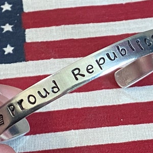May include: Silver bracelet with the words "Proud Republican" engraved on it. A small American flag is engraved on the side of the bracelet.