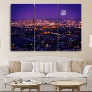 May include: A panoramic view of a city skyline at night with a large, full moon in the sky. The city is lit up with lights, and the moon casts a soft glow over the scene.