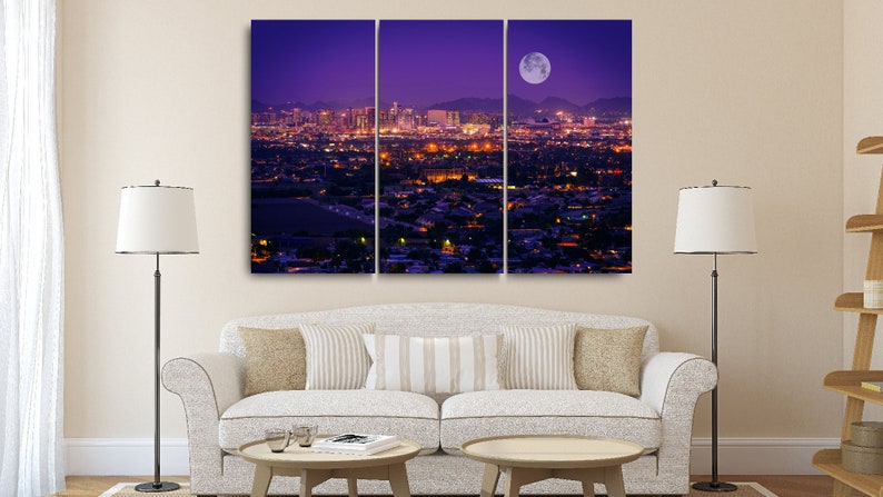 May include: A panoramic view of a city skyline at night with a large, full moon in the sky. The city is lit up with lights, and the moon casts a soft glow over the scene.