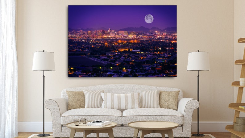 May include: A panoramic view of a city skyline at night with a full moon in the sky. The city is lit up with lights, and the mountains in the background are silhouetted against the purple sky.