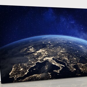 May include: A canvas print depicting a nighttime view of Earth from space, showcasing Europe and the Mediterranean Sea. City lights illuminate the land, contrasted against the dark blue of the atmosphere and a starry sky.