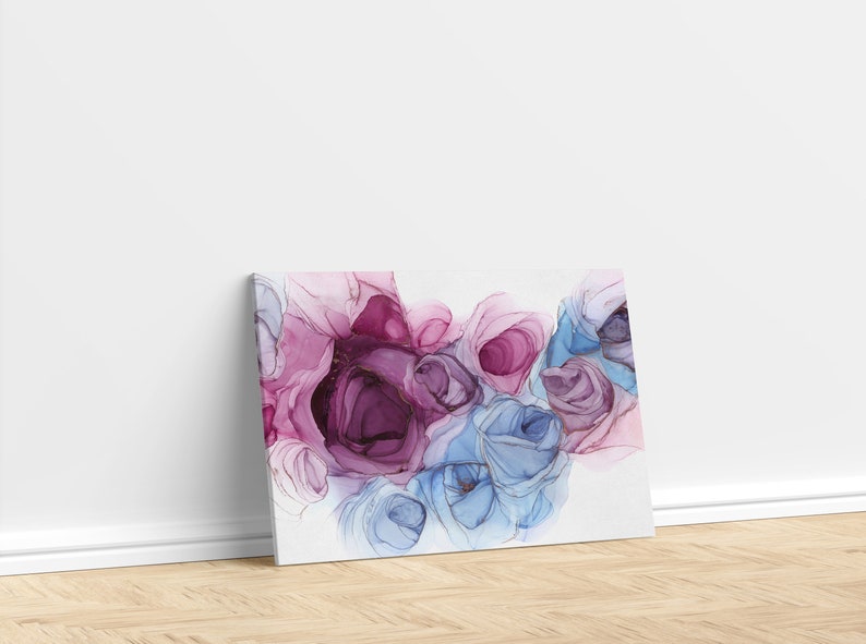May include: Canvas art print featuring an abstract floral design. The artwork showcases a cluster of stylized roses in shades of pink, purple, and blue, with gold accents. The canvas is leaning against a white wall on a wooden floor.
