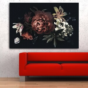 Op de afbeelding: Een groot bloemen canvas print met een donkere achtergrond, met een boeket van rode, witte en groene bloemen. Daaronder een rode bank met zilveren poten. Een zwarte vaas met decoratieve takken staat rechts.