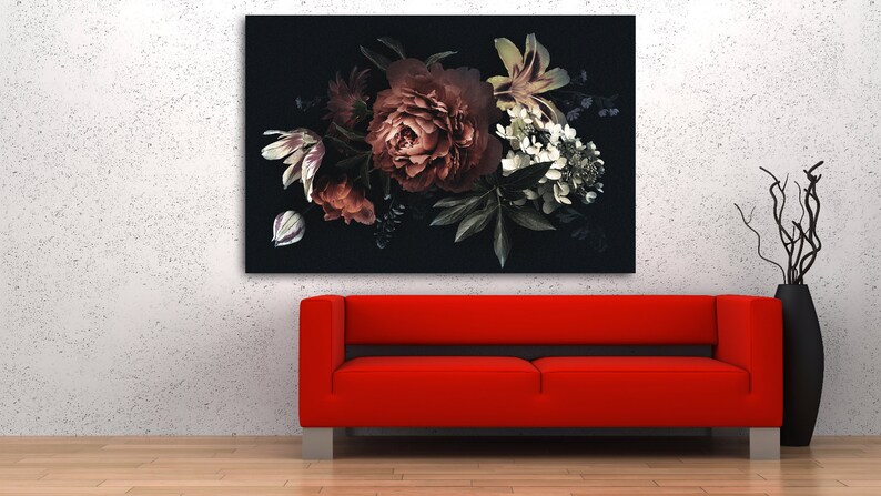 Op de afbeelding: Een groot bloemen canvas print met een donkere achtergrond, met een boeket van rode, witte en groene bloemen. Daaronder een rode bank met zilveren poten. Een zwarte vaas met decoratieve takken staat rechts.