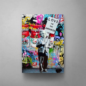 May include: A colorful graffiti art print featuring Albert Einstein holding a sign that reads "Love is the answer". The background is a vibrant mix of colors and textures, including cans of Campbell's soup.
