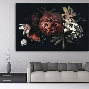 Op de afbeelding: Een canvas print met een bloemstuk tegen een donkere achtergrond. Het boeket bevat rode pioenrozen, witte lelies en groen blad. Het kunstwerk wordt tentoongesteld boven een witte bank en een zwarte kast. Afmetingen in centimeters.