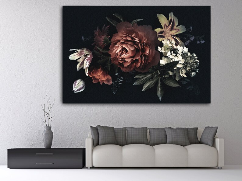Op de afbeelding: Een canvas print met een bloemstuk tegen een donkere achtergrond. Het boeket bevat rode pioenrozen, witte lelies en groen blad. Het kunstwerk wordt tentoongesteld boven een witte bank en een zwarte kast. Afmetingen in centimeters.