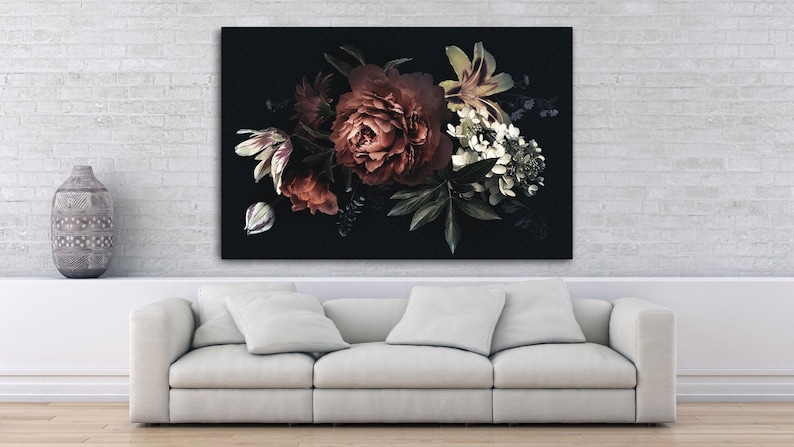 Op de afbeelding: Een groot bloemen canvas print met een donkere achtergrond, met een boeket bloemen in rood, wit en groen. De print wordt weergegeven boven een witte bank in een woonkamer.