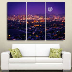 May include: A three-panel canvas print depicting a cityscape at night with a full moon in the sky. The city is lit up with lights, and the moon casts a soft glow over the scene.