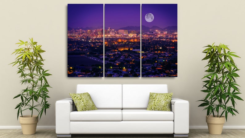 May include: A three-panel canvas print depicting a cityscape at night with a full moon in the sky. The city is lit up with lights, and the moon casts a soft glow over the scene.