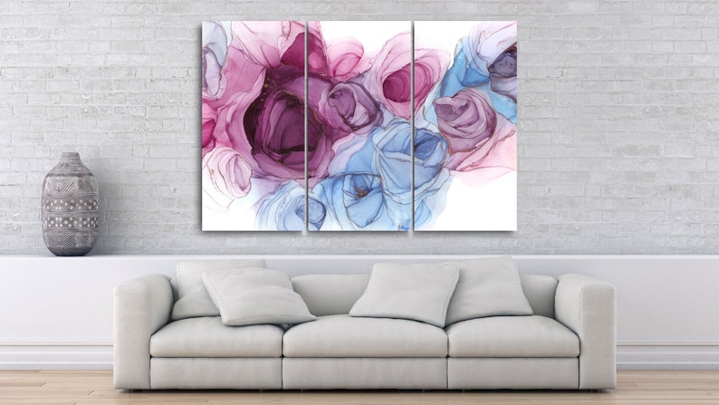 May include: Triptych canvas art featuring abstract floral designs in shades of purple, pink, and blue. The artwork is displayed above a white sofa in a modern living room setting. The background is a white brick wall.
