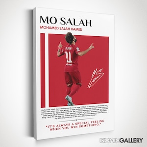 May include: A framed print featuring Mo Salah in a red soccer uniform, arms raised in celebration. The print has the text "MO SALAH" and "MOHAMED SALAH HAMED" at the top. The background is red with white vertical stripes.