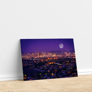 May include: A nighttime cityscape with a full moon in the sky. The city is lit up with lights, and the buildings are silhouetted against the purple sky.