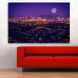 May include: A nighttime cityscape with a full moon in the sky. The city is lit up with lights, and the mountains in the distance are silhouetted against the purple sky.