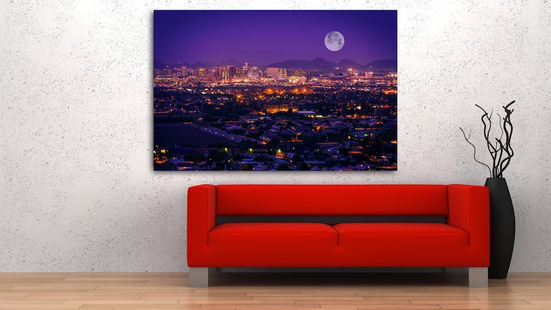 May include: A nighttime cityscape with a full moon in the sky. The city is lit up with lights, and the mountains in the distance are silhouetted against the purple sky.