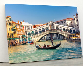 May include: A gondola with a gondolier and passengers floats on a canal in Venice, Italy. The Rialto Bridge is in the background.