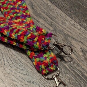 May include: A colorful, hand-crocheted lanyard with a vibrant mix of red, orange, yellow, green, purple, and blue yarn. The lanyard features two silver-colored swivel clasps for attaching keys or an ID badge.