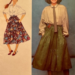 May include: Two women wearing different outfits with a similar skirt style. The woman on the left is wearing a white blouse with a floral skirt. The woman on the right is wearing a plaid shirt with a green skirt. Both women are wearing a brown belt with a buckle.