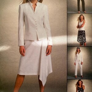 May include: A white blazer with a mandarin collar and a white skirt with a diagonal hemline. The skirt is asymmetrical and has a long, flowing hem on one side. The blazer has a button closure and a fitted silhouette. The model is wearing white heels.