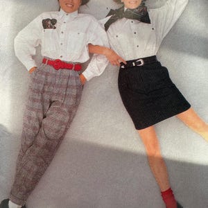 May include: Two women wearing white button-down shirts, one with a red belt and plaid pants, the other with a black belt and a black skirt. Both are wearing black shoes and red socks.