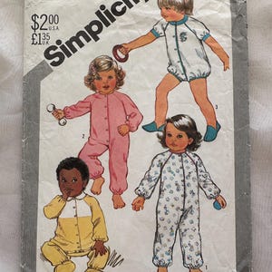 May include: A Simplicity sewing pattern envelope 5593 for toddler clothing. The cover features illustrations of four children wearing various styles of one-piece rompers and pajamas in pink, yellow, white with blue trim, and a white patterned fabric.
