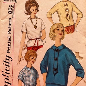May include: A vintage sewing pattern for four different blouses. The pattern is for a junior size 11 with a bust measurement of 31 1/2 inches. The pattern is printed on a pink background with a white border. The pattern includes instructions and diagrams for sewing the blouses. The blouses are shown on four different models. The first blouse is a white blouse with a short sleeve and a tie belt. The second blouse is a blue and white plaid blouse with a short sleeve and a collar. The third blouse is a light yellow blouse with a three-quarter sleeve and a button-up front. The fourth blouse is a blue blouse with a three-quarter sleeve and a button-up front.