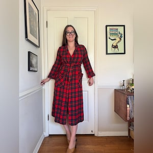May include: A red and black plaid robe with long sleeves and a tie waist. The robe has two front pockets and is knee-length. The robe is made of a soft, woven fabric. The robe is a classic and comfortable garment.