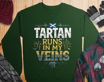 May include: A dark green sweatshirt with the text "TARTAN RUNS IN MY VEINS" in white and yellow, with a Scottish flag graphic. The design includes a heartbeat line and a tartan pattern.