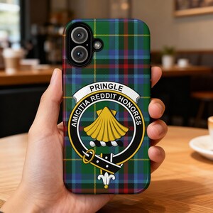May include: A smartphone case featuring a green, blue, and red plaid pattern. The case has a crest with the words "PRINGLE REDDIT HONORES" and a gold scallop shell design. The case is held in a person's hand.