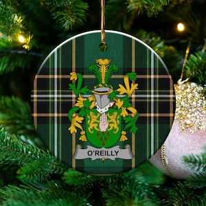 May include: A round ceramic ornament featuring a green and black tartan plaid background. Centered is a heraldic crest with a silver helmet, green shield, two gold lions, a red hand, and a banner at the bottom with the text O'REILLY.