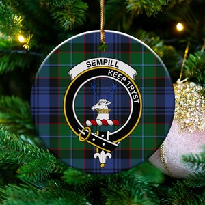 May include: Circular Christmas decoration with a green, blue, and red tartan design. The ornament displays a crest with a deer and the words "SEMPILL" and "KEEP TRYST". A gold string is attached for hanging.