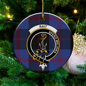 May include: Round Christmas ornament with a blue, red, and white plaid pattern. The ornament features a crest with the name "RAIT" and the motto "SPERO MELIORA". A gold cord is attached for hanging.